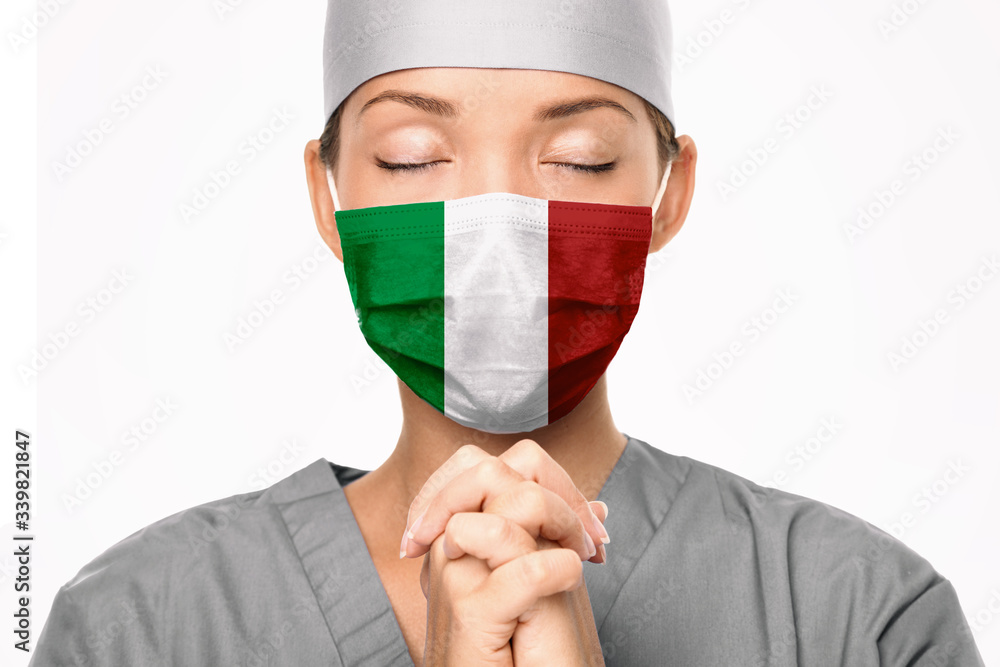 Italy flag print on surgical mask. Doctor praying for help. Young Asian woman medical doctor praying for Italy. Coronavirus pandemic outbreak in Italy. Italy flag print on surgical mask. Doctor praying for help. Young Asian woman medical doctor praying for Italy. Coronavirus pandemic outbreak in Italy.