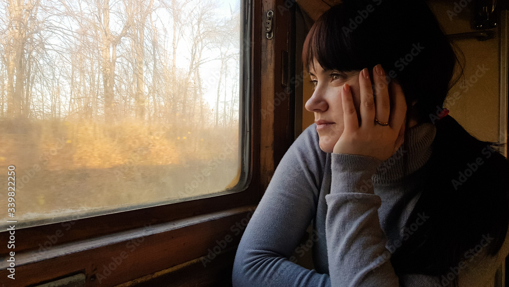 Young pretty woman traveling on a classic train sitting near the window. vintage filter. Girl tourist looks out the window of a moving old train, enjoying travel and natural beautiful scenery