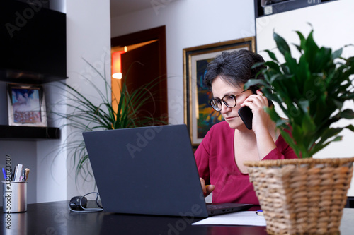 Donna Bianca con i capelli scuri e maglia colorata lavora in modalità smart working da casa sua  photo