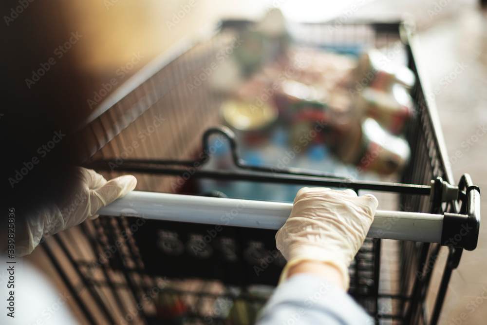 Woman wearing gloves to prevent coronavirus while using a shopping cart Woman wearing gloves to prevent coronavirus while using a shopping cart