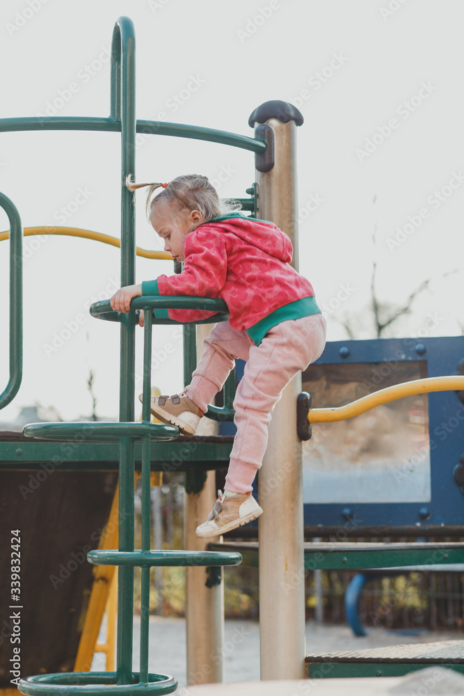 A child on the Playground with a cute face on a natural background. A little girl with blond hair pulled back in ponytails. Beauty, dexterity, hairstyle. The concept of a happy childhood.