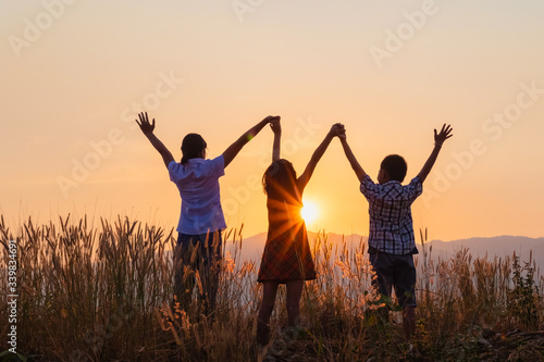 Silhouette of happy children standing with raised hands on the mountain at the sunset time.