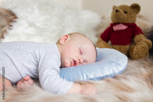 Little baby boy sleeping on a sofa on artificial fur, with teddy bear