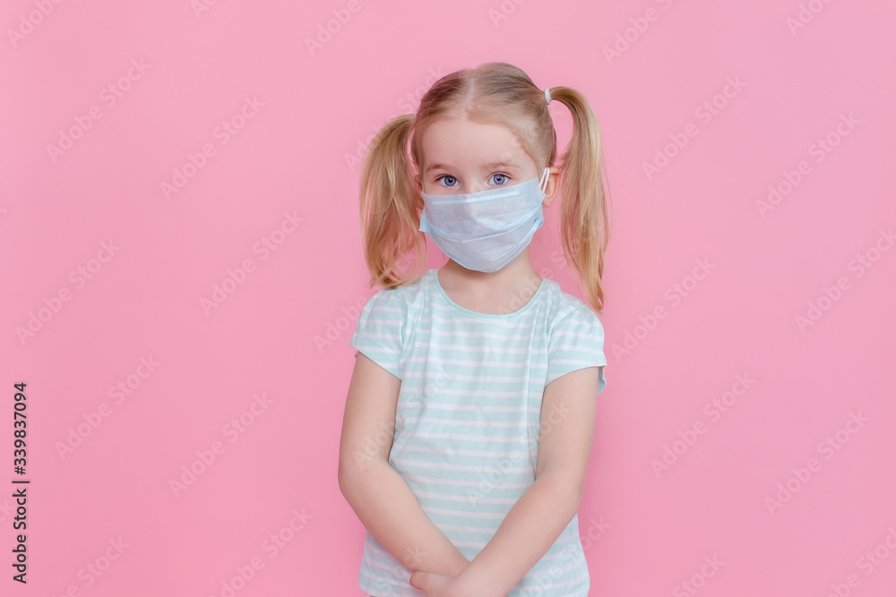 Little blonde girl with two ponytales in a medical mask face on a pink background looking at the camera