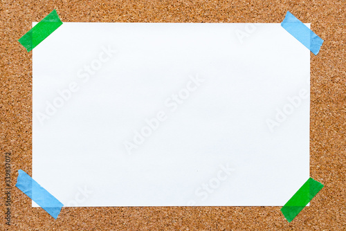 Empty paper sheet with white texture and green masking tape on  brown cork board surface. Copy space for add text or art work designs.