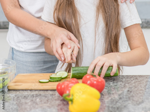 Closeup mom teaches her daughter to cut cucumbers for vegetable salad