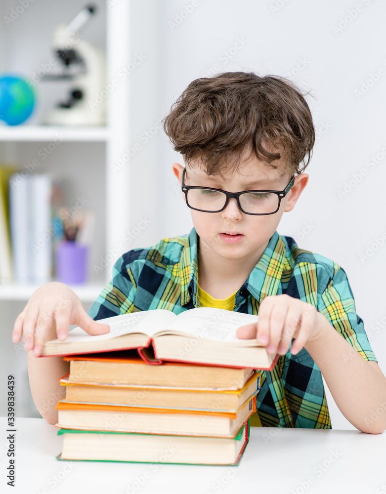 Smart boy wearing eyeglasses reads book at school Smart boy wearing eyeglasses reads book at school