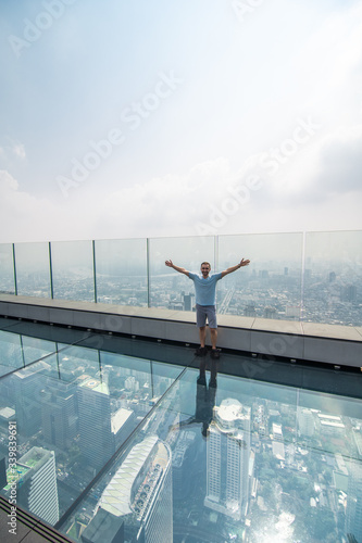 Photography Young man with raised haands on a glass floor on the roof of a King Power Mahana