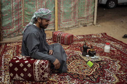 Obraz na płótnie Bedouin man wearing traditional clothes watches a footbal match in a smartphone on a carpet in the Saudi desert w salonie