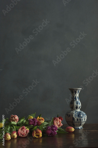 Delft blue vase with pink, yellow, red and purple tulips on wooden table.