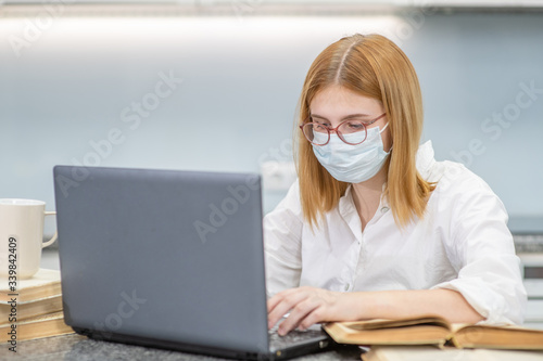 Teen girl wearing medical mask is engaged in distance learning with a laptop. Quarantine and coronavirus epidemic concept