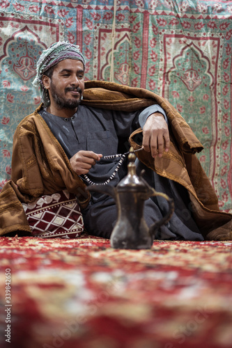 Obraz na płótnie Bedouin man wearing traditional clothes praying with a tasbih while drinking tea on a carpet in the Saudi desert w salonie