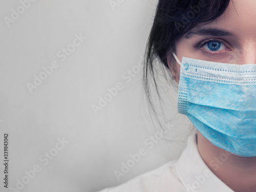 Portrait of a young European woman in a protective disposable medical mask. Concept of caronavirus Cavid 19 and human quarantine. Girl in a mask on a white wall. Masked medical worker. photo