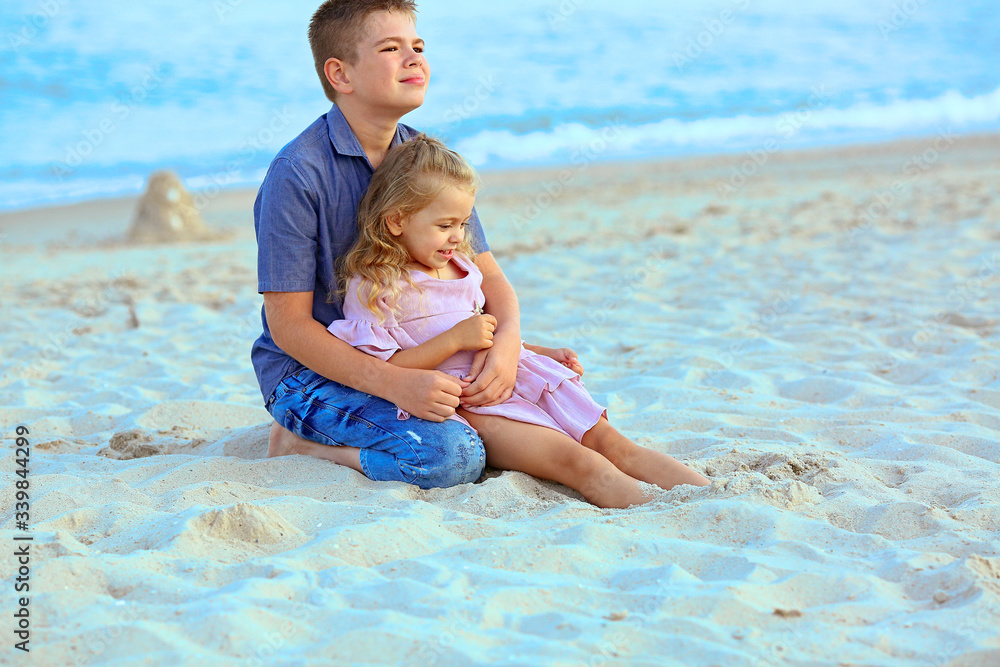 Beautiful Caucasian kids are sitting on the beach. A boy in a blue shirt, girl in a pink dress. Rest and travel. Family day. Happy family concept.
People and advertising concept Beautiful Caucasian kids are sitting on the beach. A boy in a blue shirt, girl in a pink dress. Rest and travel. Family day. Happy family concept.
People and advertising concept