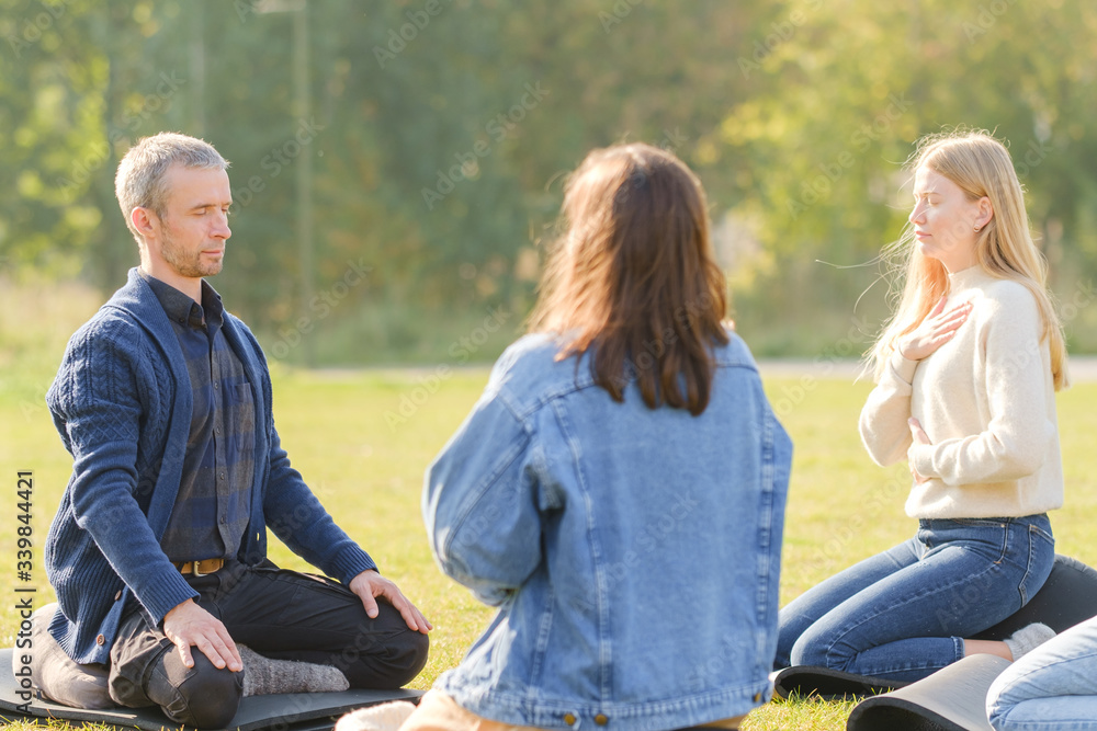 A group of young people meditate outdoors in a park. A group of young people meditate outdoors in a park.