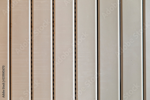 Close-up on a radiator composed of vertical heating panels. They are white and worn and have interstices made up of small holes