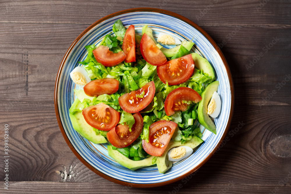 salad with tomatoes, green leaves, eggs, avocado in blue plate on brown wooden background salad with tomatoes, green leaves, eggs, avocado in blue plate on brown wooden background