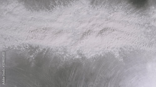 Closeup of the hand of a man throwing wheat flour on a metallic table in slow motion.