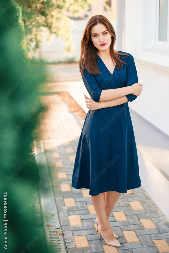 Red-haired model in a dark blue dress posing in the garden. Red-haired model in a dark blue dress posing in the garden.