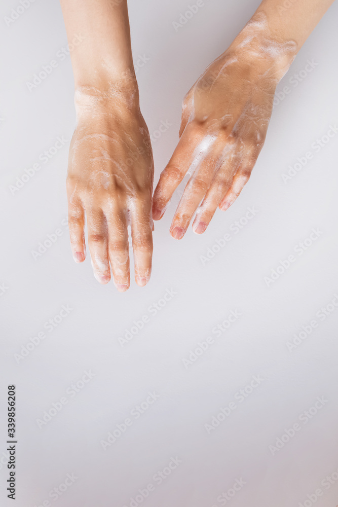 Fototapeta premium Feminime hands with soapy bubbly foam on white wall background