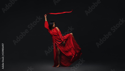 Dancer in red dress dancing in the dark studio