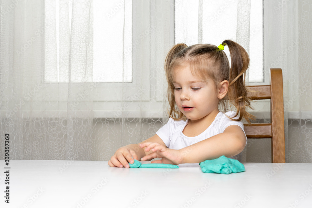 girl preschooler sits at a table and sculpts from turquoise dough for tepka. activities with children at home on self-isolation in connection with coronavirus infection girl preschooler sits at a table and sculpts from turquoise dough for tepka. activities with children at home on self-isolation in connection with coronavirus infection