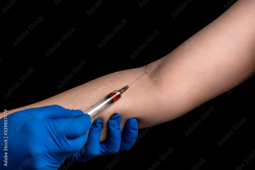 a doctor in disposable gloves takes blood from a patient’s vein for analysis on a black background a doctor in disposable gloves takes blood from a patient’s vein for analysis on a black background
