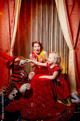 Family during a stylized theatrical circus photo shoot in a beautiful red location. Models mother and daughter posing on stage with curtain