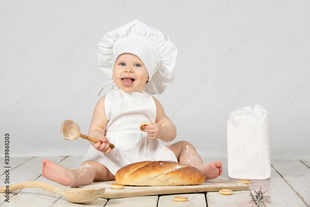 Child cook. Beautiful little girl in cook clothes with long loaf and flour. The child is one year old. Funny baby is laughing. Little chef. The concept of baking bakery products. Child cook. Beautiful little girl in cook clothes with long loaf and flour. The child is one year old. Funny baby is laughing. Little chef. The concept of baking bakery products.