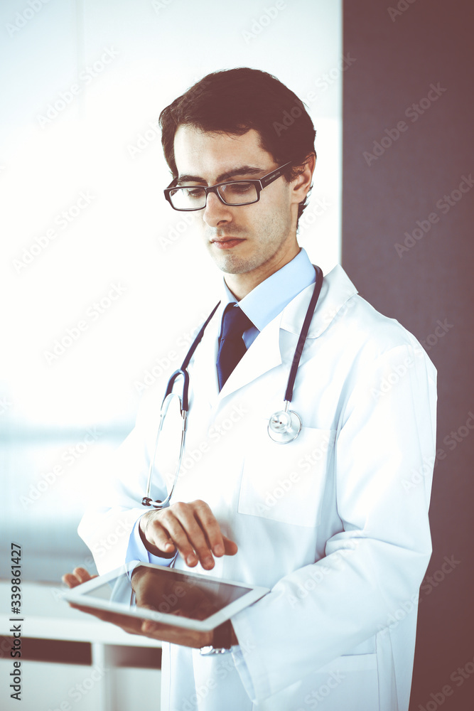 Fototapeta premium Doctor man using tablet computer for network research or virtual disease treatment. Perfect medical service in clinic. Modern medicine, medic data and healthcare concepts