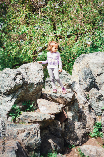 A little girl in a t-shirt and pants climbs on rocks  mountains  peaks  conquering peaks  game  Park  forest  adventure with family  learning geography  terrain