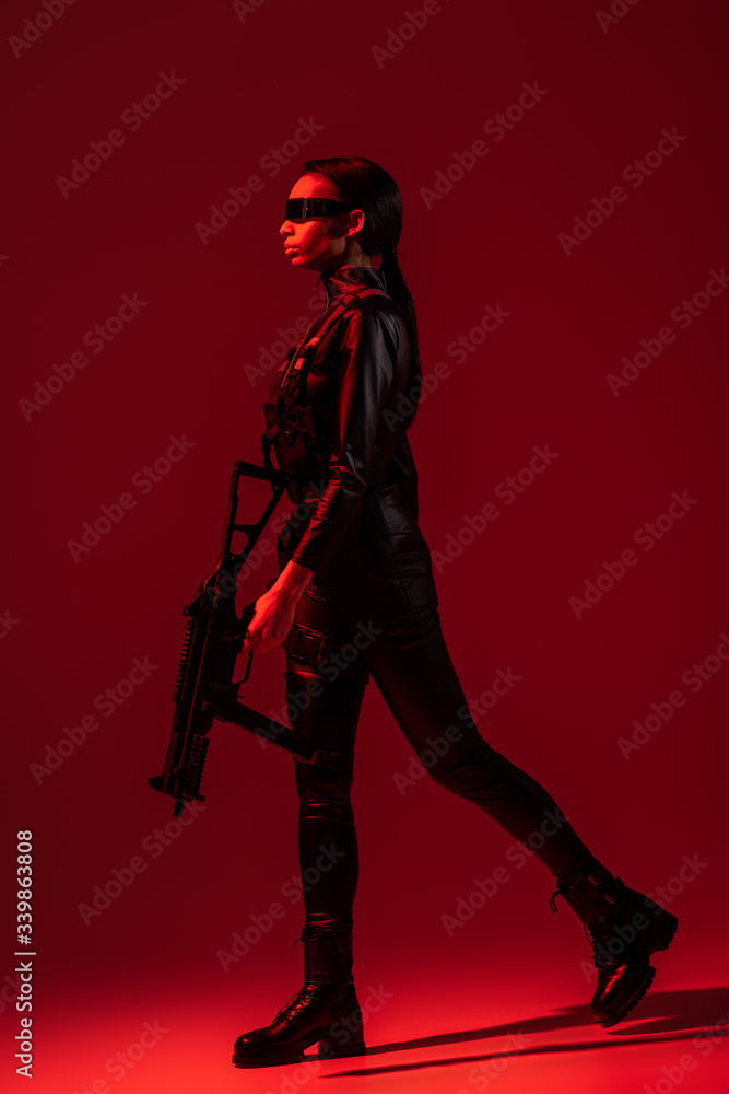 futuristic african american woman in glasses walking with assault rifle on red background futuristic african american woman in glasses walking with assault rifle on red background