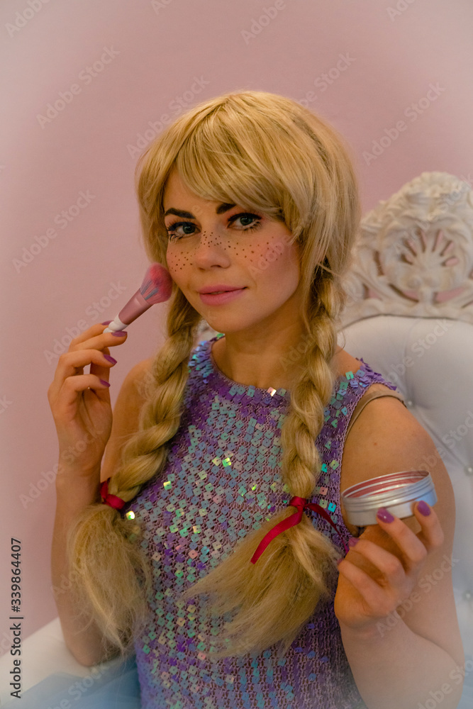 Lady in the doll costume makes makeup, blush. A wig and a beautiful elegant dress for a thematic holiday. Lady in the doll costume makes makeup, blush. A wig and a beautiful elegant dress for a thematic holiday.