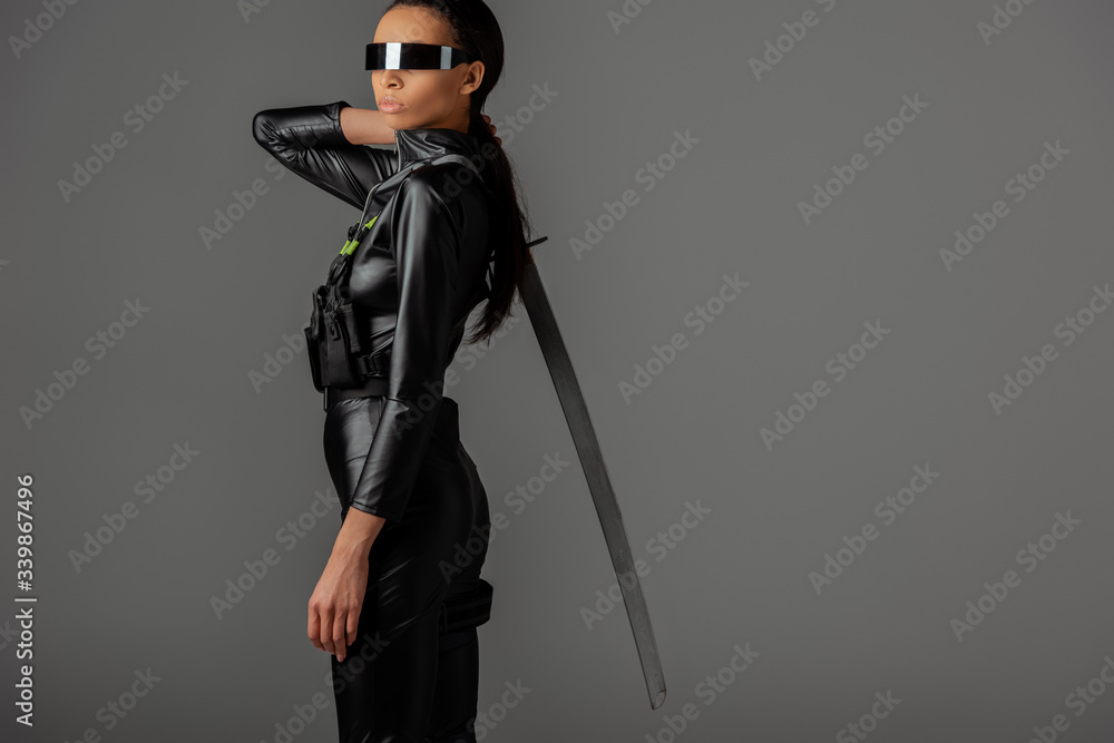 side view of futuristic african american woman in glasses with sword on grey side view of futuristic african american woman in glasses with sword on grey