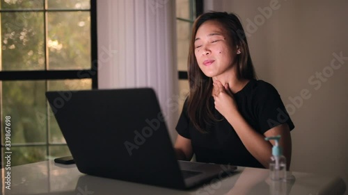 Asian woman working from home having soar throat rubbing the neck. Stay home and social distancing to avoid corona virus. Focus work on the laptop.