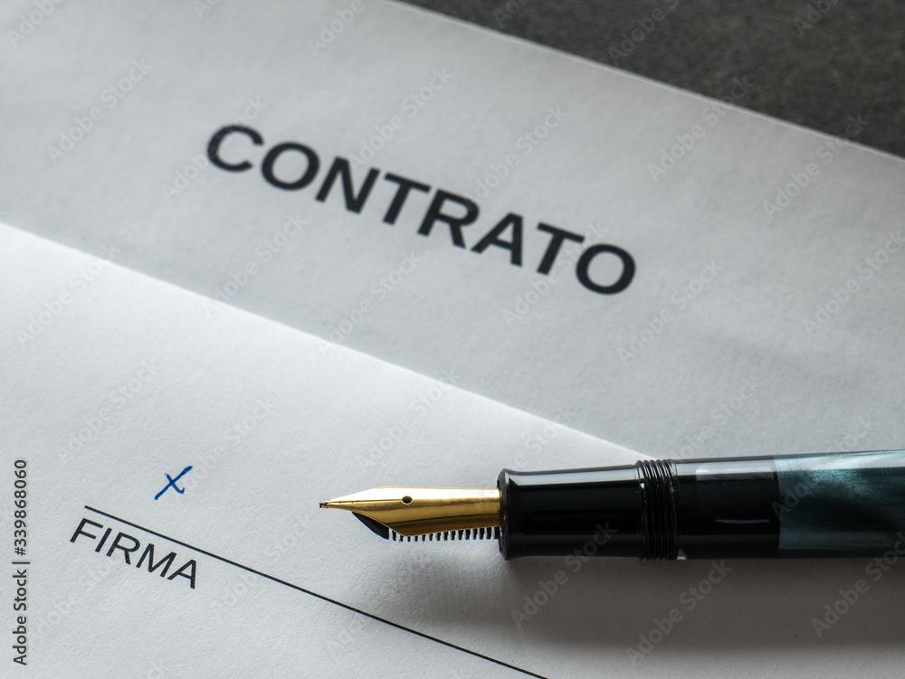 Symbolic pen and sheet of paper on a desk showing the text CONTRACT in Spanish, below there is a line for signing and the Spanish word for SIGNATURE Symbolic pen and sheet of paper on a desk showing the text CONTRACT in Spanish, below there is a line for signing and the Spanish word for SIGNATURE