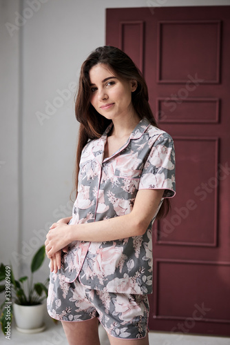 Canvas Print Young pretty slim brunette woman, wearing colorful light pink and grey pajamas with flowers pattern, posing for picture in front of claret marsal wall