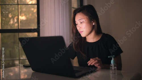Asian lady cleaning the laptop with wet wipes and tissue to avoid spread of coronavirus. Social distancing and work focus on laptop. Hand gel sanitizer on the table.