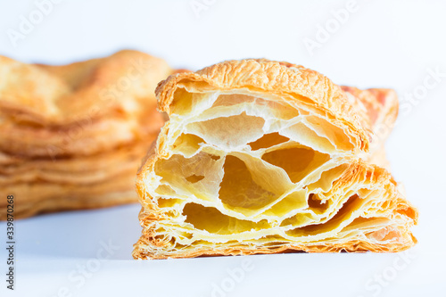 A closeup image  of puff pastry in the incision with blown large crunchy layers of golden brown crust on top visible. Located on a white background