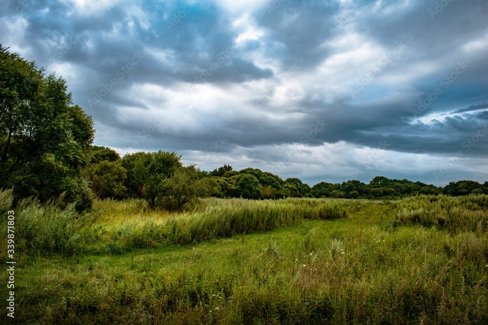 Landscape with thunderclouds over a green field and hills