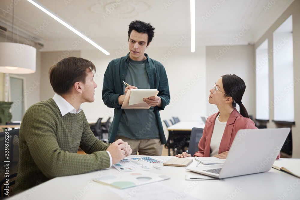 Group of financial advisors sitting at the table and listening to their manager during a meeting at office Group of financial advisors sitting at the table and listening to their manager during a meeting at office