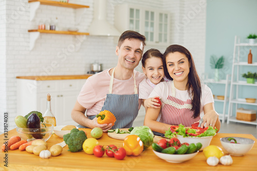 Happy family with daughter in the kitchen with vegetables look at the camera.