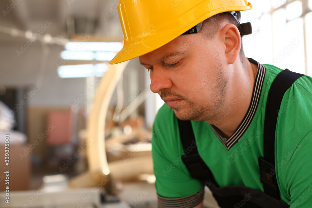 Portrait of young attractive man in work clothes and yellow helmet crossed arms smiling at shop for manufacturing furniture and details home interior Portrait of young attractive man in work clothes and yellow helmet crossed arms smiling at shop for manufacturing furniture and details home interior