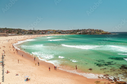 Bondi Beach Sydney holiday scene. Famous vacation spot in city, with beautiful ocean, sun, sea and sand. Tourists sunbathing on beach, with waves washing in. Australia.