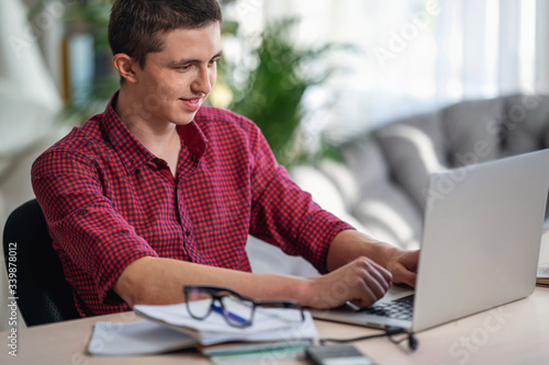 Smiling active teen guy watching a training video. does homework using a laptop