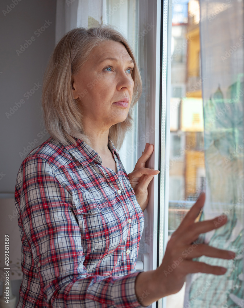 Fototapeta premium The woman in the room by the window. He looks sadly at the street. Quarantine. Loneliness.