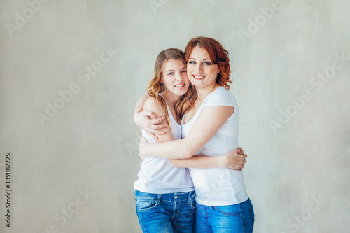 Stay at home mom, stay safe. Young mother embracing her child. Woman and teenage girl relaxing in white bedroom near gray wall indoors. Happy family at home. Young mom playing whith her daughter.