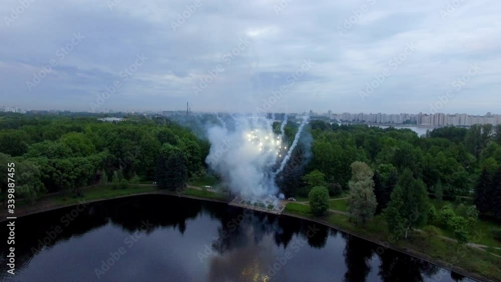 Aerial view of Festive Salute above the lake in park at evening. Several salvos of golden fireworks in sky.
Aerial view of Festive Salute above the lake in park at evening. Several salvos of golden fireworks in sky.