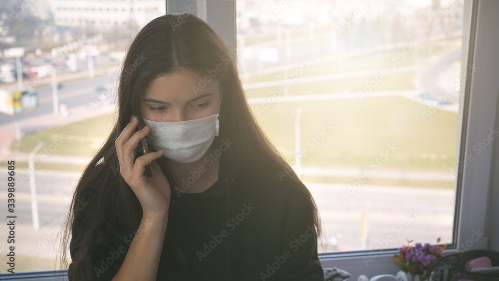teen girl in medical face mask talking by smartphone siting on table teen girl in medical face mask talking by smartphone siting on table
