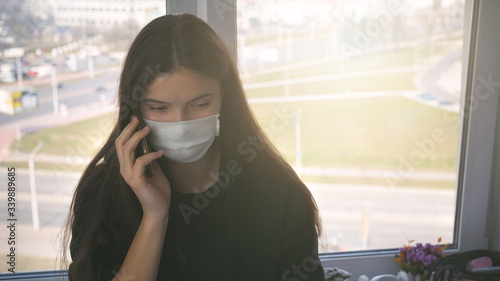 teen girl in medical face mask talking by smartphone siting on table